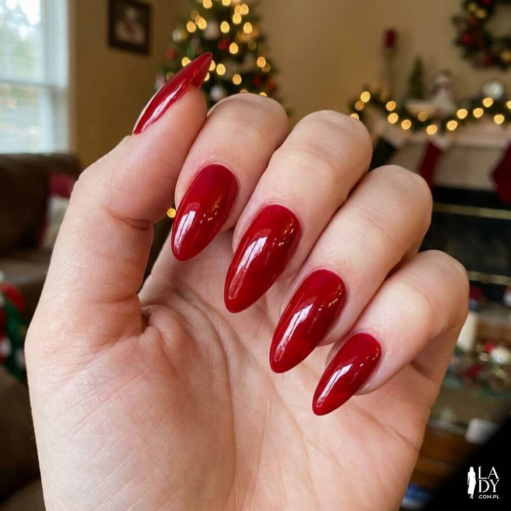 Zbliżenie na dłoń z czerwonymi paznokciami o wysokim połysku imitującym taflę szkła na świątecznym tle