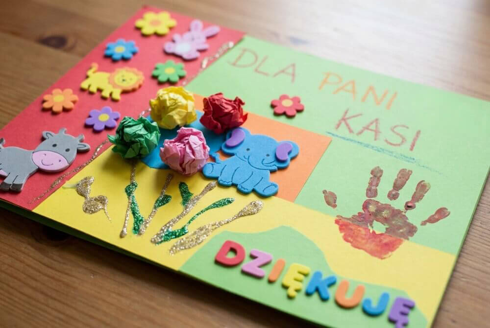 Ozdobiona laurka z elementami bibułki, brokatu i odicsków, leżąca na stole 