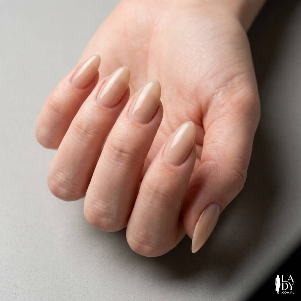 Zbliżenie na dłoń kobiety z paznokciami w kształcie migdałków po piłowaniu, w neutralnym manicure nude