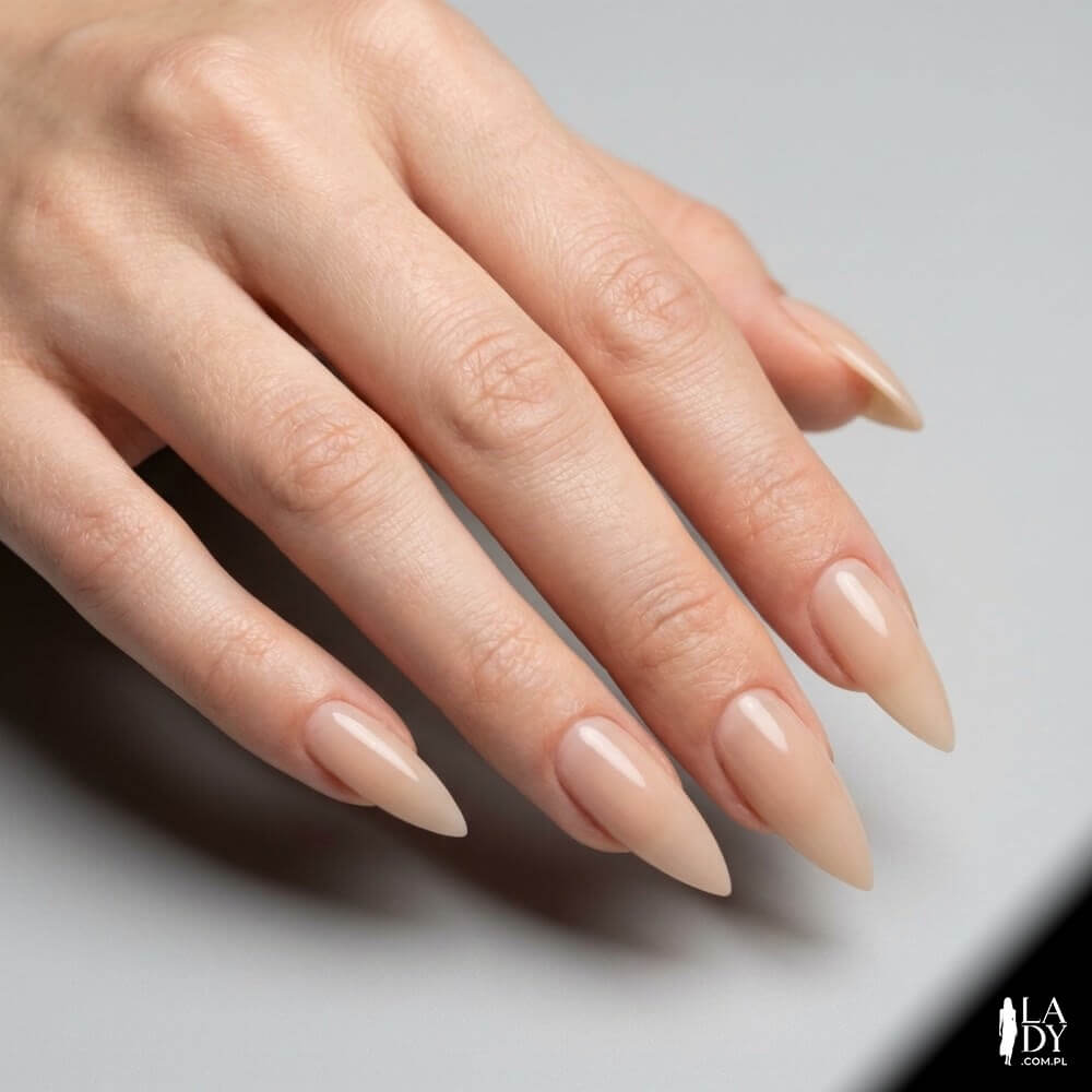Zbliżenie na dłoń kobiety z paznokciami w kształcie szpica (stiletto) po piłowaniu, w neutralnym manicure nude