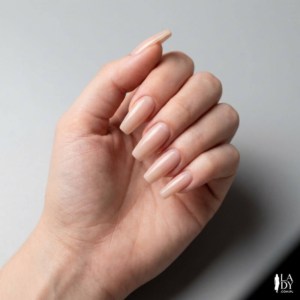 Zbliżenie na dłoń kobiety z paznokciami w kształcie trumienek (coffin) po piłowaniu, w neutralnym manicure nude