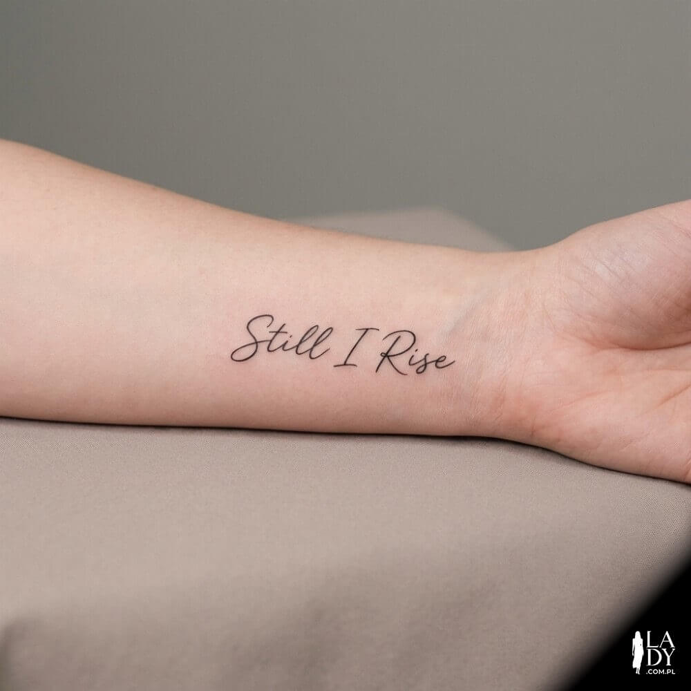 Tatuaż z napisem „Still I Rise” na ręce kobiety w neutralnym, studyjnym kadrze