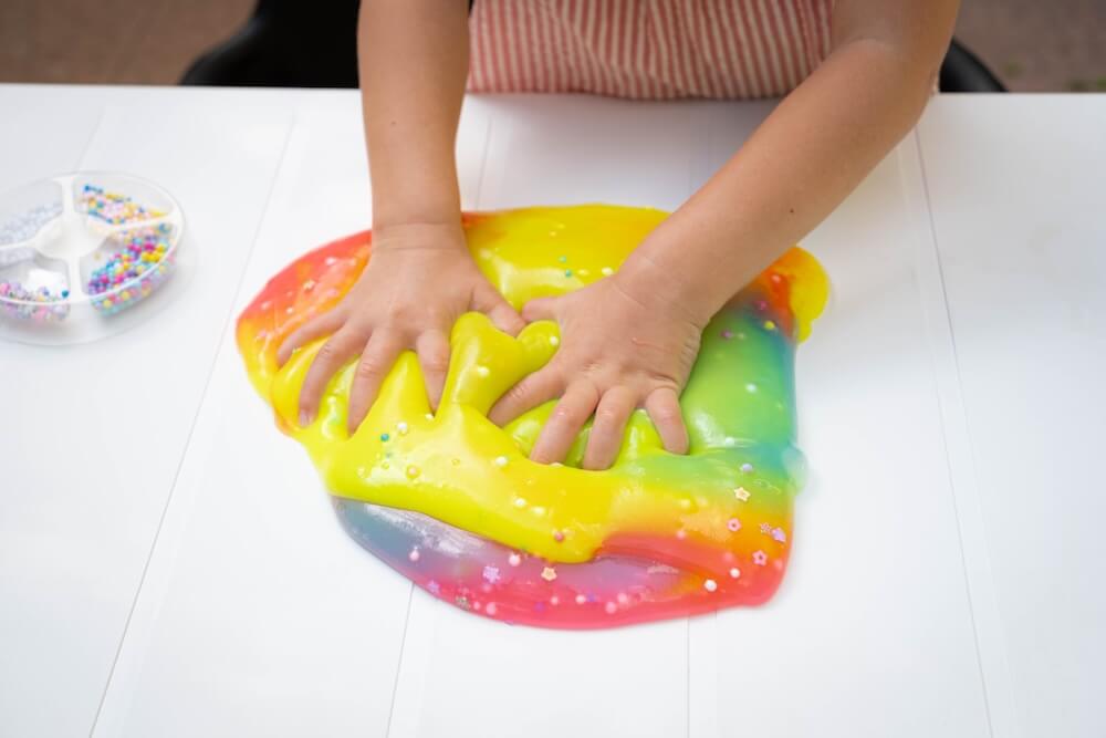 Tęczowy slime z kuleczkami i brokatem wyrabiany przez dziecko