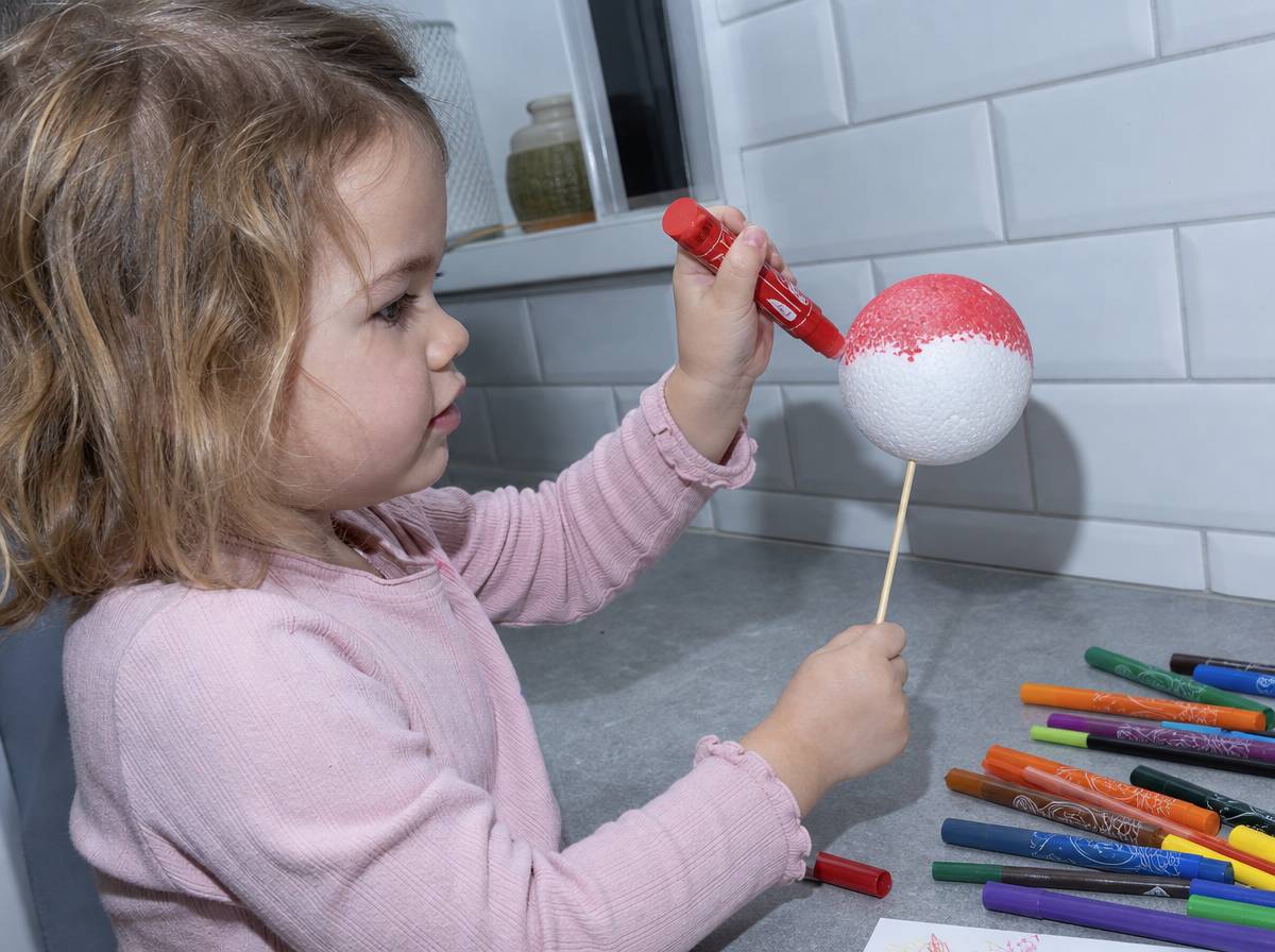 Dziecko maluje kulę styropianową farbą w sztyfcie na bombkę DIY