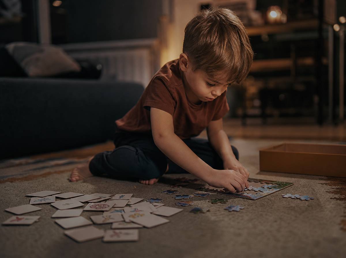 Dziecko układa puzzle na dywanie obok domowych kart memory