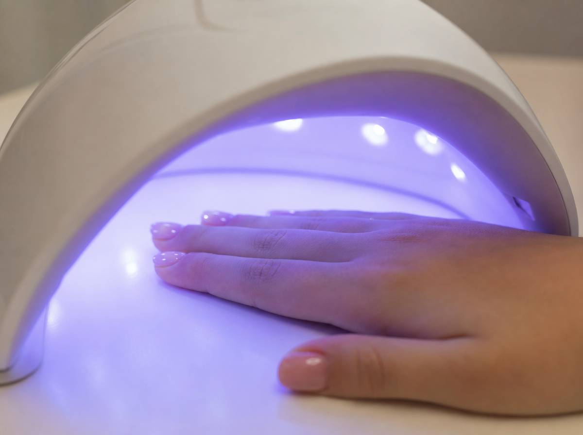 Dłoń nastolatki pod lampą UV podczas utwardzania żelowej powłoki na paznokciach.